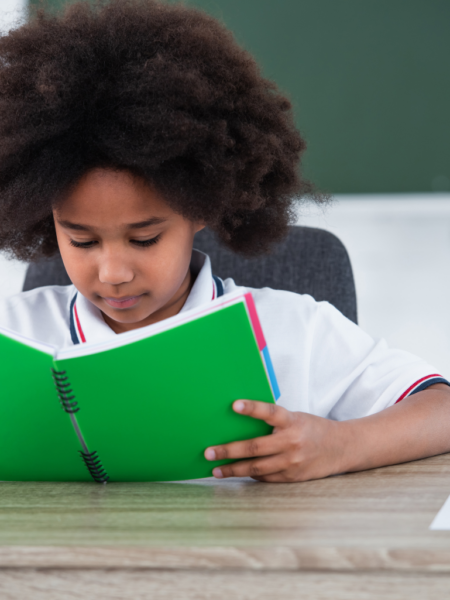 Menina lendo livro na educação infantil em sala de aula, representando o desenvolvimento da leitura e contação de histórias alinhada à BNCC