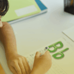 Criança em fase de alfabetização escrevendo letras em atividade lúdica com material didático do Sistema Etapa Público em sala de aula.