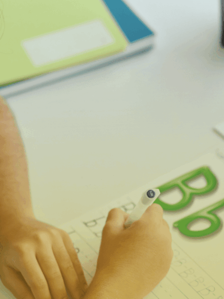 Criança em fase de alfabetização escrevendo letras em atividade lúdica com material didático do Sistema Etapa Público em sala de aula.