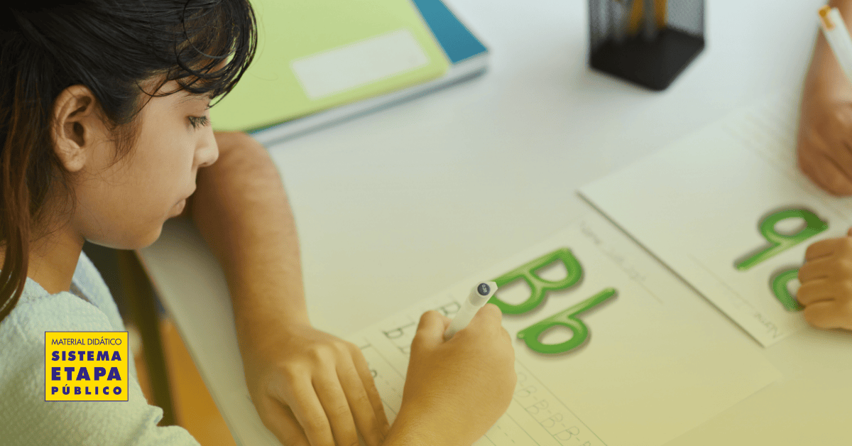 Criança em fase de alfabetização escrevendo letras em atividade lúdica com material didático do Sistema Etapa Público em sala de aula.
