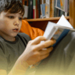 Criança lendo um livro em uma biblioteca, promovendo a cultura literária com livros recomendados para estimular o hábito de leitura.