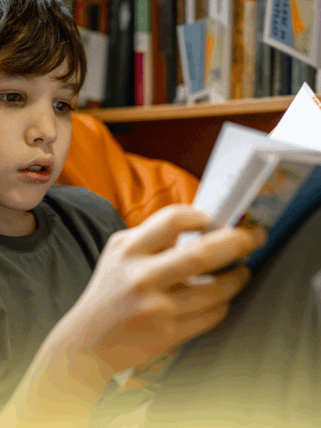 Criança lendo um livro em uma biblioteca, promovendo a cultura literária com livros recomendados para estimular o hábito de leitura.