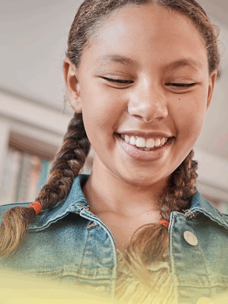 Estudante sorrindo enquanto lê um livro em uma biblioteca escolar, representando o incentivo à leitura durante as férias.