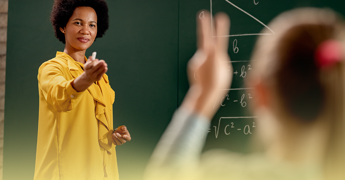 Professora da escola pública conduz a aula e incentiva a participação dos alunos, que levantam a mão durante atividade em sala de aula.