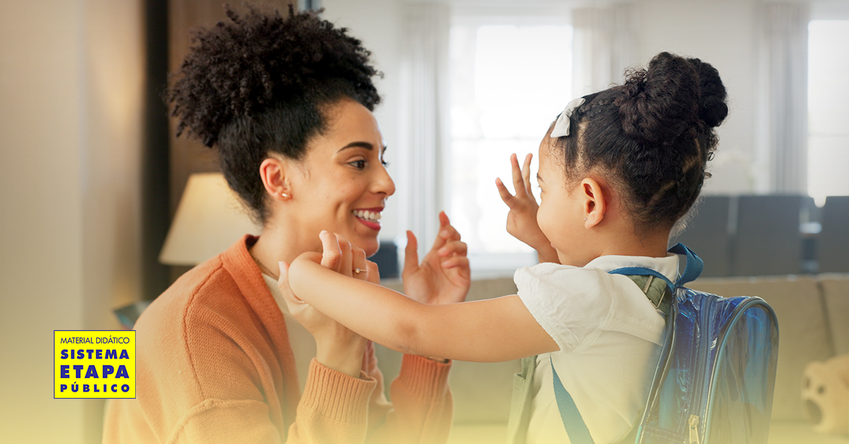 Mãe se despede da filha antes de ir para a escola, demonstrando carinho, atenção e envolvimento na vida escolar da criança.