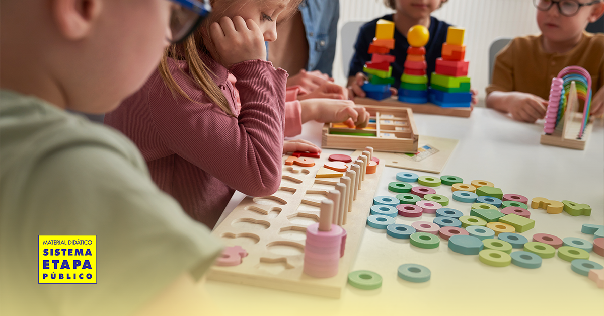 Crianças da Educação Infantil participam de atividades lúdicas com jogos de encaixe, blocos coloridos e materiais pedagógicos, em um ambiente escolar acolhedor e colaborativo.