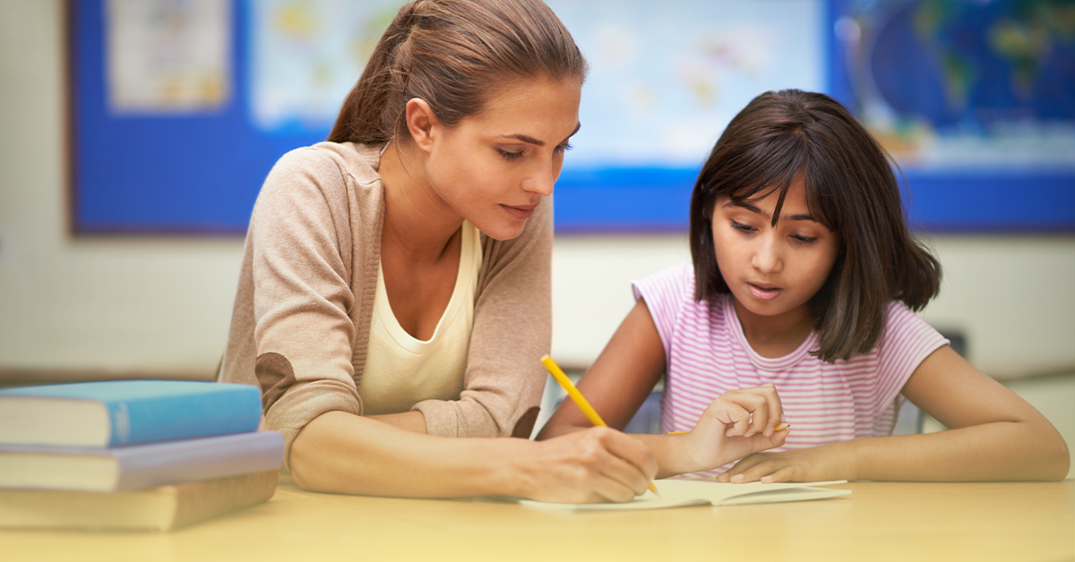 Professora auxiliando aluna em atividade escolar, representando o papel da mulher na educação e a importância do Dia Internacional da Mulher no ambiente escolar.