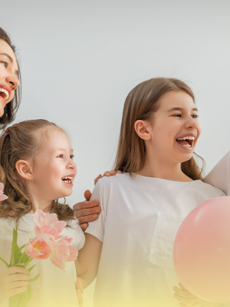Três gerações de mulheres — avó, mãe e filhas — sorrindo e segurando flores em celebração ao Dia Internacional da Mulher, representando união, respeito e valorização feminina na educação.