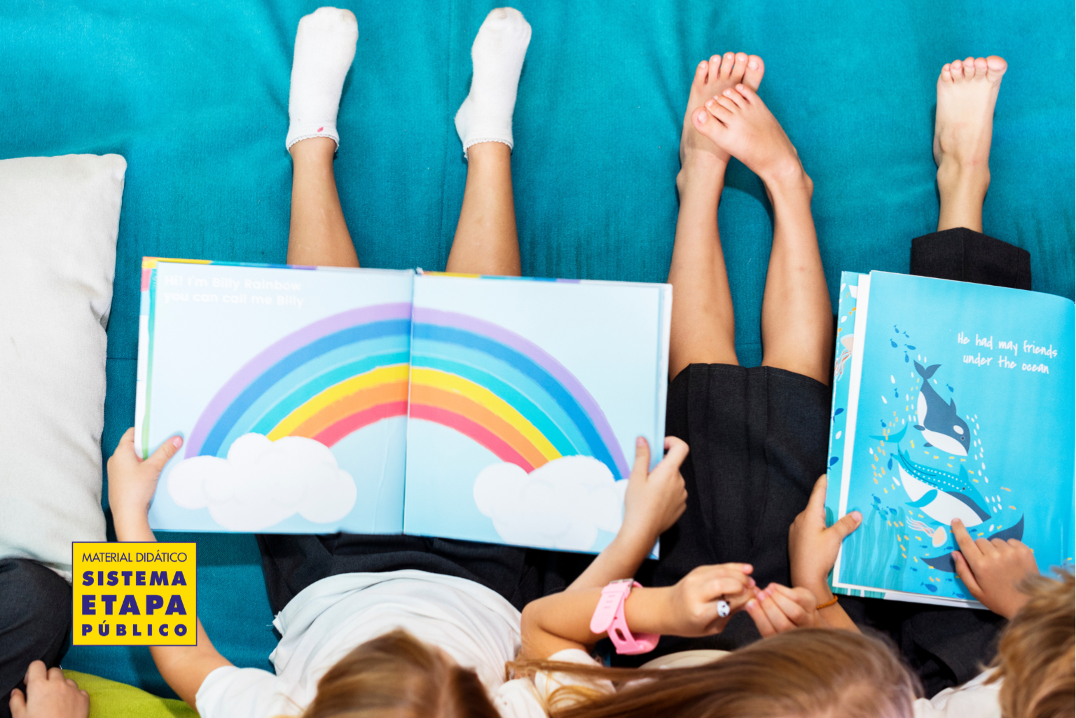 Crianças lendo livros infantis coloridos juntas, deitadas no chão, explorando histórias ilustradas que estimulam a imaginação e o desenvolvimento da leitura.