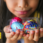 Criança segurando ovos de Páscoa coloridos em embalagem, representando atividades escolares relacionadas à Páscoa e ao aprendizado lúdico.