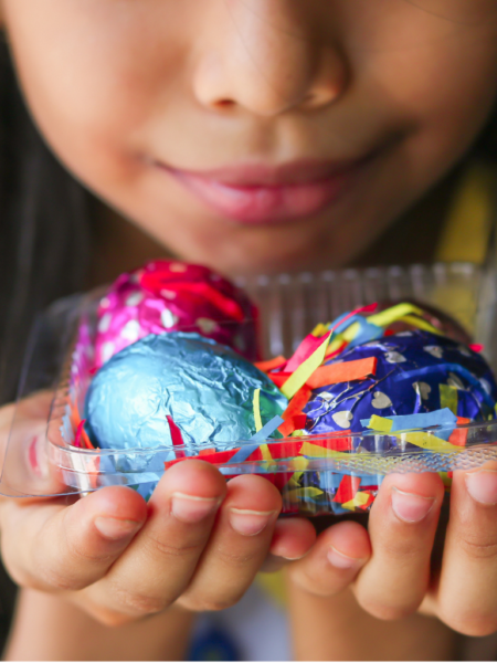 Criança segurando ovos de Páscoa coloridos em embalagem, representando atividades escolares relacionadas à Páscoa e ao aprendizado lúdico.